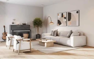 A bright, minimalist living room featuring a modern and musical aesthetic. On the right, a large, light beige modular sofa is styled with grey and patterned throw pillows, sitting against a white wall adorned with two large framed abstract art prints in earthy tones of beige, black, and peach. A sleek floor lamp with an arched stem and a brass shade provides accent lighting near the art. In the center, a light wood, geometric low coffee table rests on a large textured beige area rug, holding a couple of books. Two cream-colored armchairs with light wood frames are positioned facing the table on the left. Behind them, against the back wall, sits a dark grey upright piano with a few small decor items resting on top, and an acoustic guitar stands on a floor stand to its left. A tall, bushy green potted plant stands between the piano and the sofa, adding a touch of nature. The room features light wood flooring, recessed ceiling lights, and soft natural light creating gentle shadows.